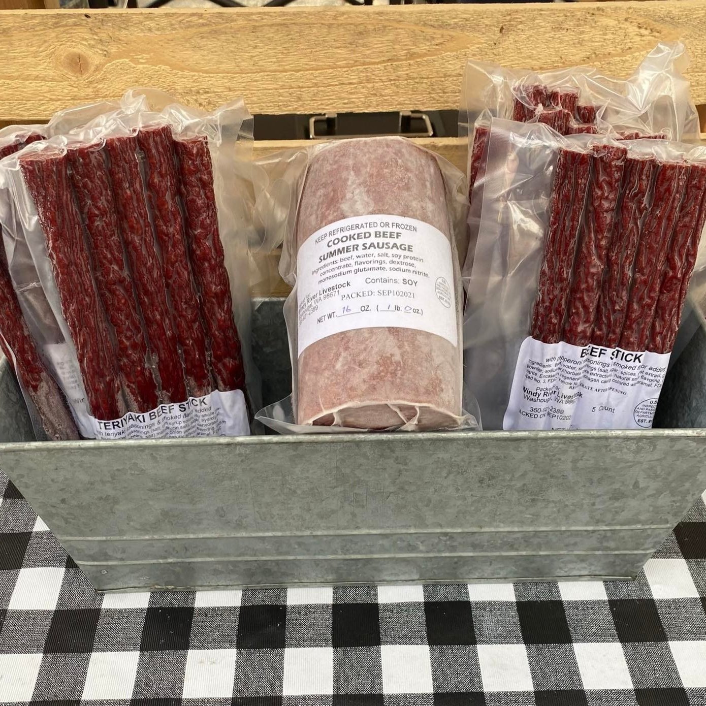 Assorted beef snacks in a metal container, featuring packages of teriyaki beef sticks, beef sticks, and cooked beef summer sausage, all labeled with nutritional information and storage instructions.